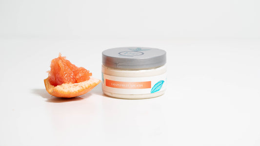 A 4 oz. jar of Grapefruit Splash Whipped Body Butter and small piece of grapefruit is displayed against a pristine white background.