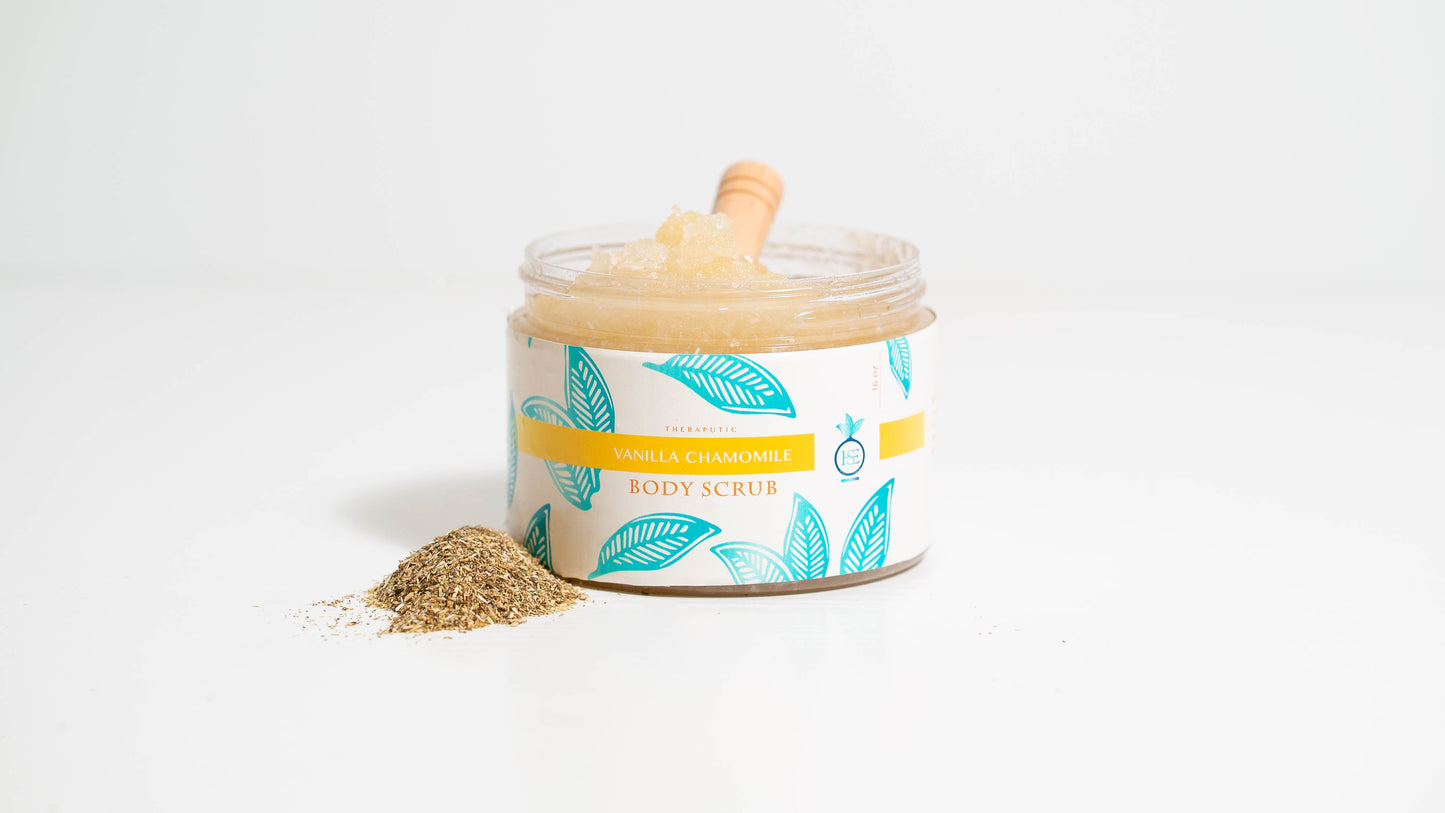 A 16 oz. jar of Vanilla Chamomile body scrub is positioned against a white background, featuring a wooden scooper nestled inside the jar, highlighting the scrub's natural ingredients and soothing aroma.